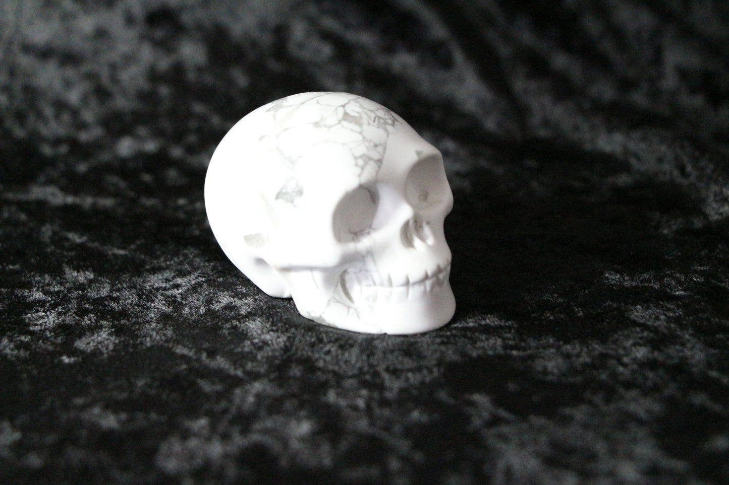 White marble skull sculpture with gray veins on black textured fabric background