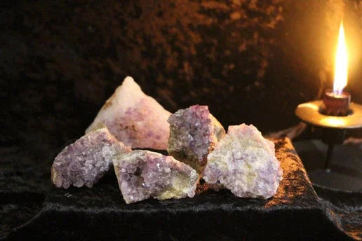 Cluster of raw amethyst crystals on black velvet next to a lit candle in a dark setting