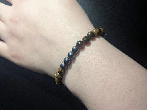 Close-up of a wrist wearing a beaded bracelet with black and brown gemstone beads on black background
